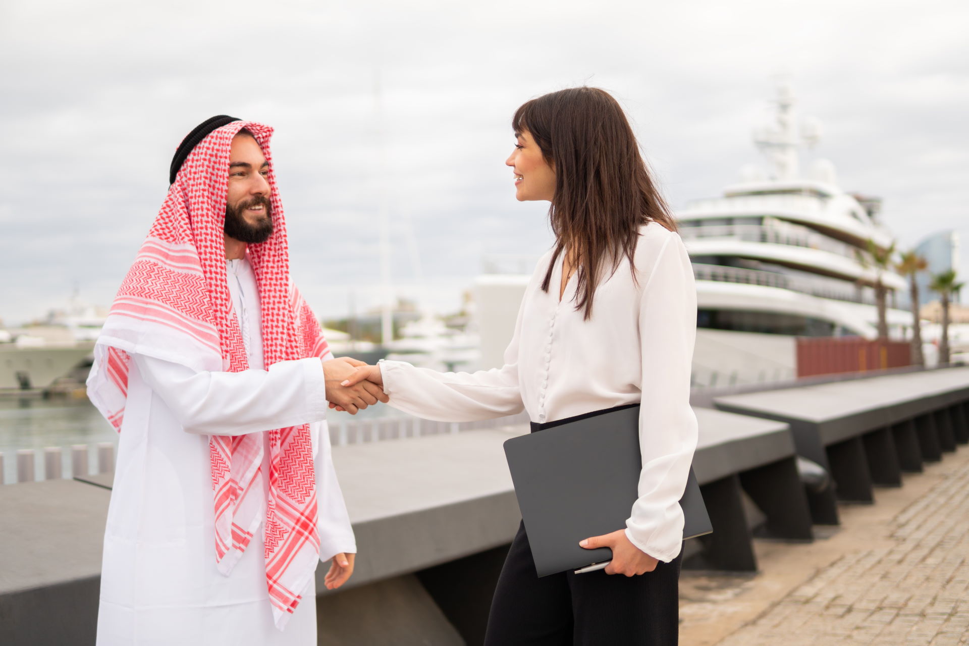 Ein Mann mit Turban schüttelt im Yachthafen einer Geschäftsfrau die Hand