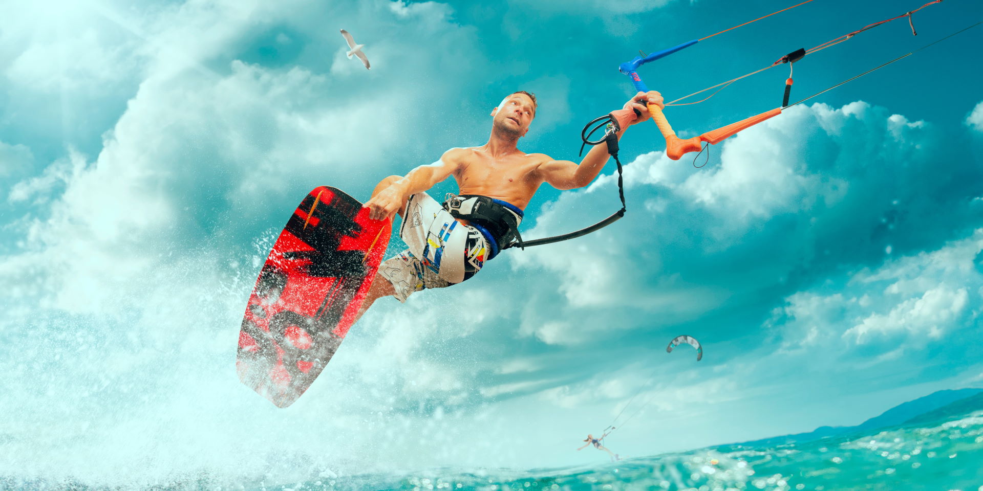 İyi bronzlaşmış atletik bir adam yüksek bir dalganın üstünde uçurtma sörfünün halatını tutuyor.