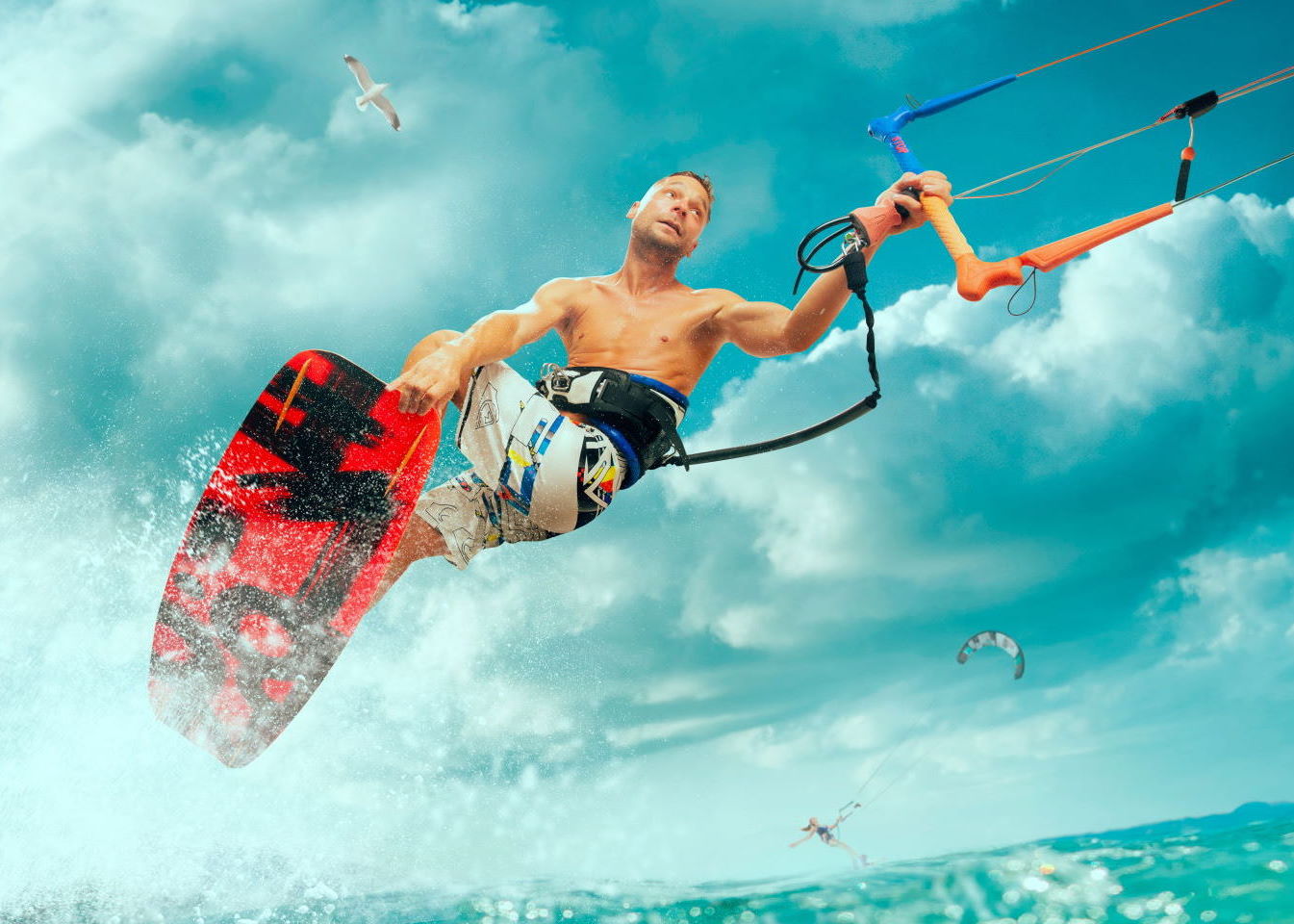A well-toned athletic man is kitesurfing on a high wave and holding on to the rope
