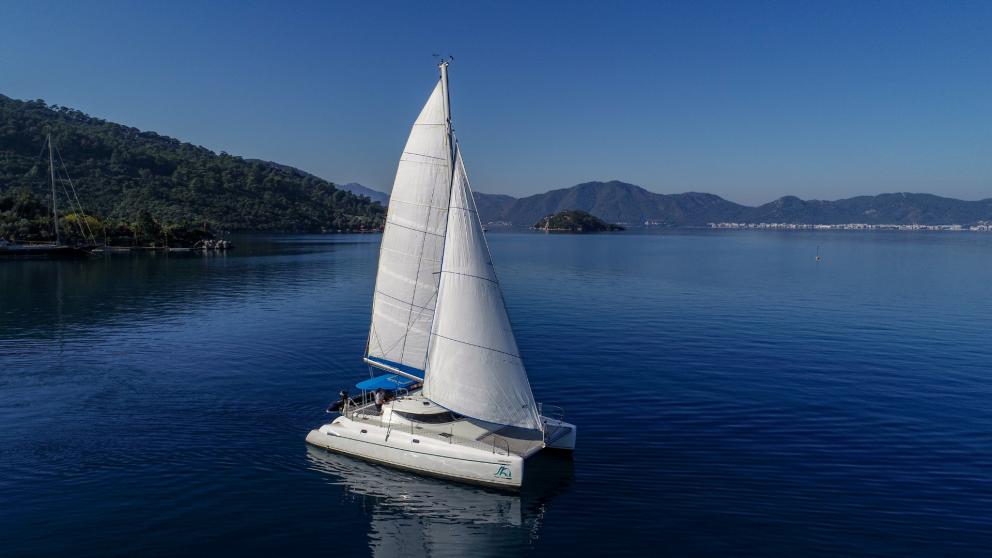 Rented catamaran with raised sails Andromeda at sea surrounded by mountains
