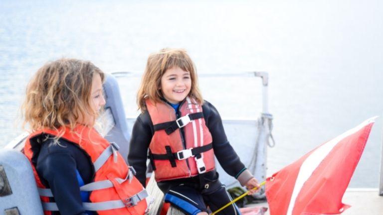 Two girls are travelling on the boat wearing life jackets.