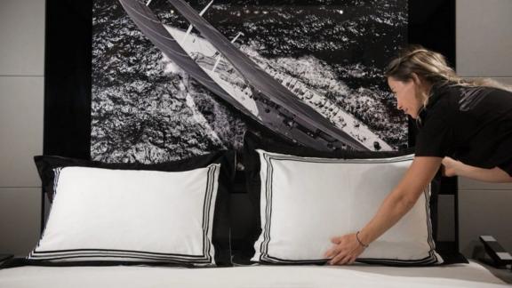 The hostess straightens the bed of a luxury yacht for rent, and the boat image on the headboard is in harmony with the p